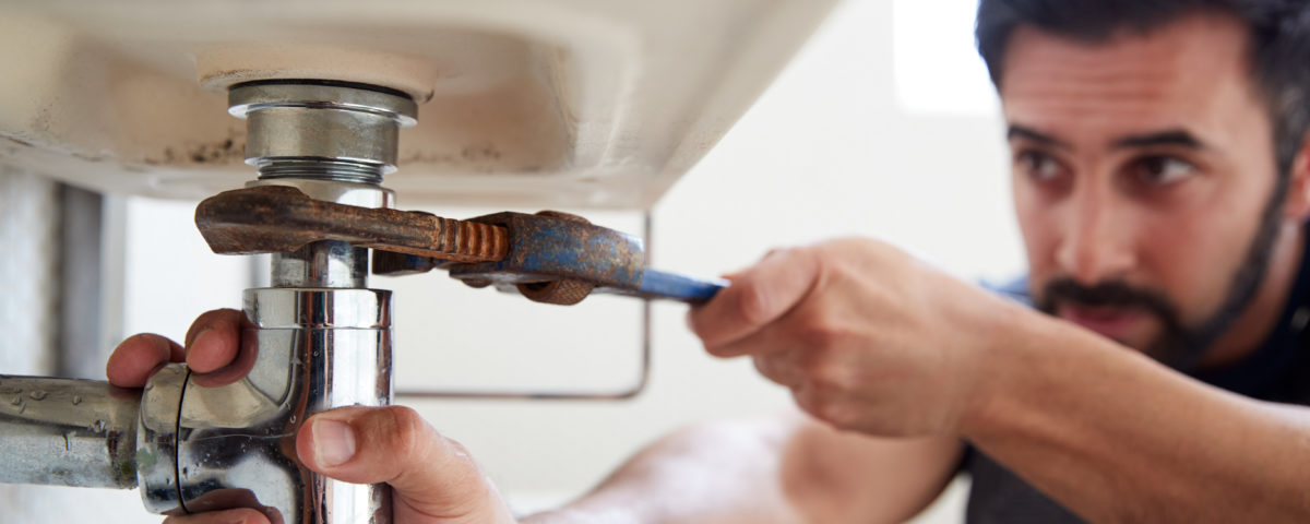 male plumber using wrench to fix leaking sink in h UQGLNG7 1200x480 1